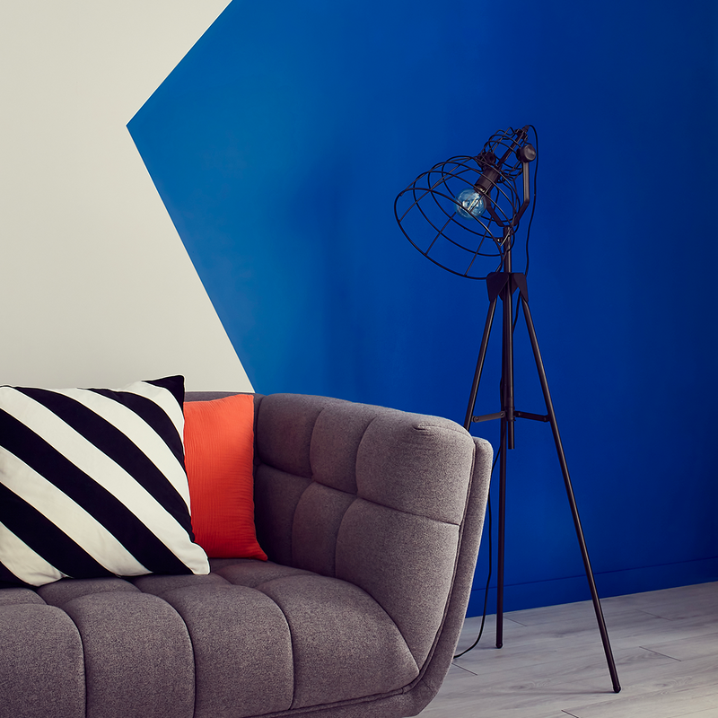 Mur bicolore bleu électrique et blanc, avec canapé gris et coussins noir et blanc et orange