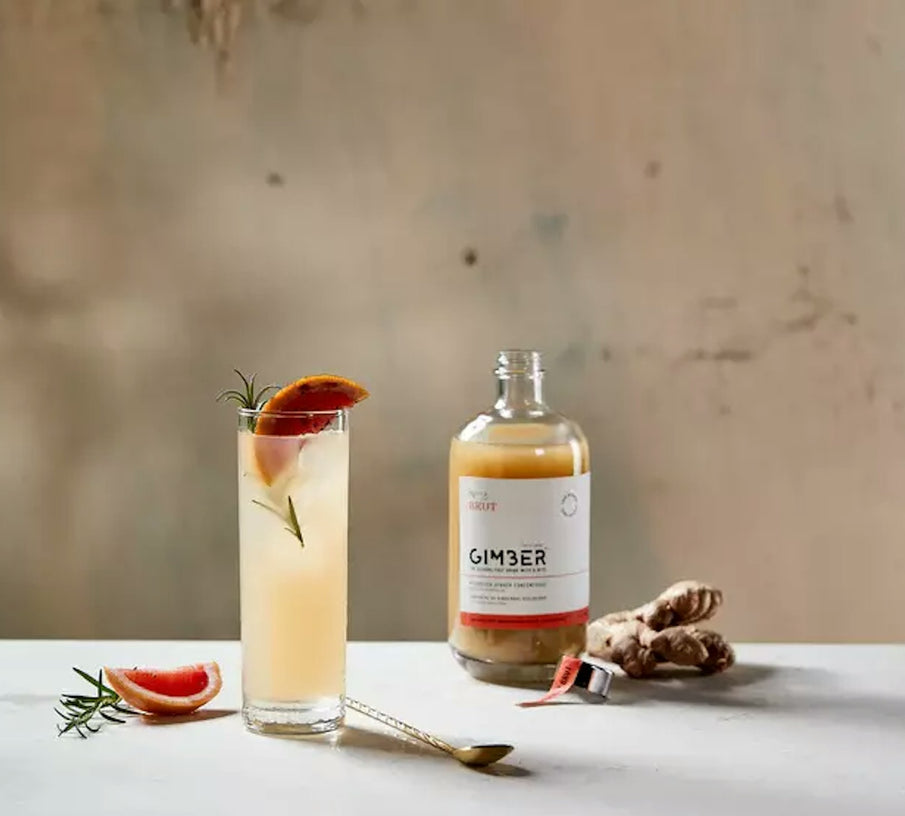 Verre à cocktail rempli d'une boisson apéritive sans alcool au gingembre, orange sanguine et romarin, bouteille de concentré de gingembre bio de la marque Gimber