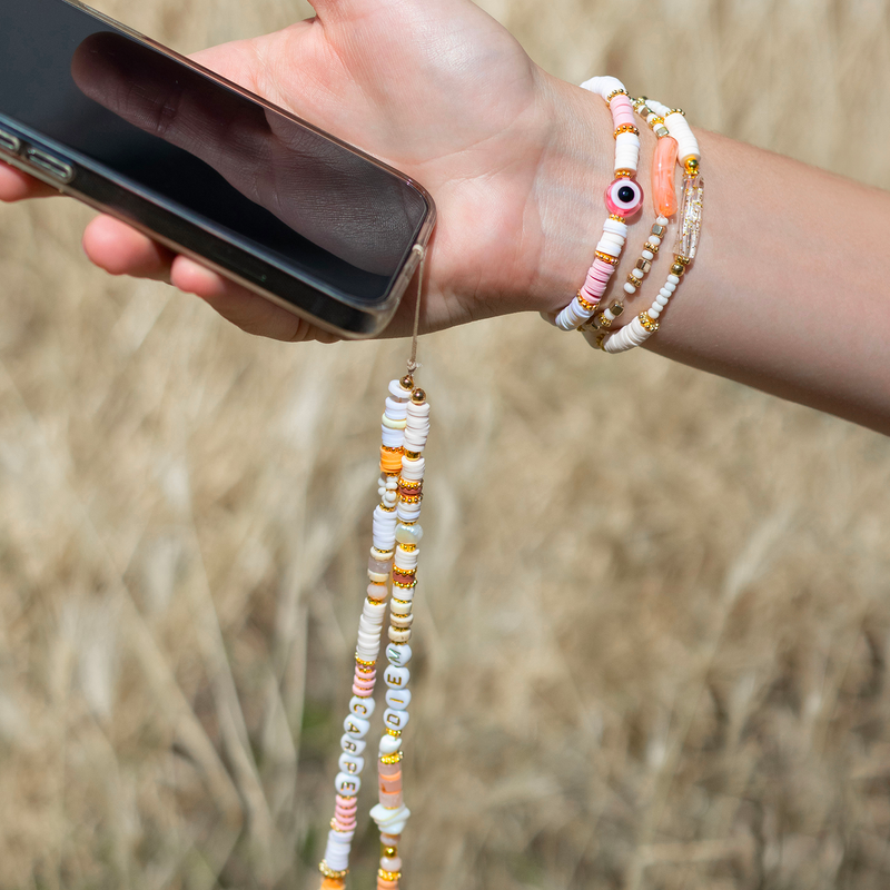 Main tenant un téléphone avec des bracelets de perles au poignet et un cordon de téléphone en perles heishi