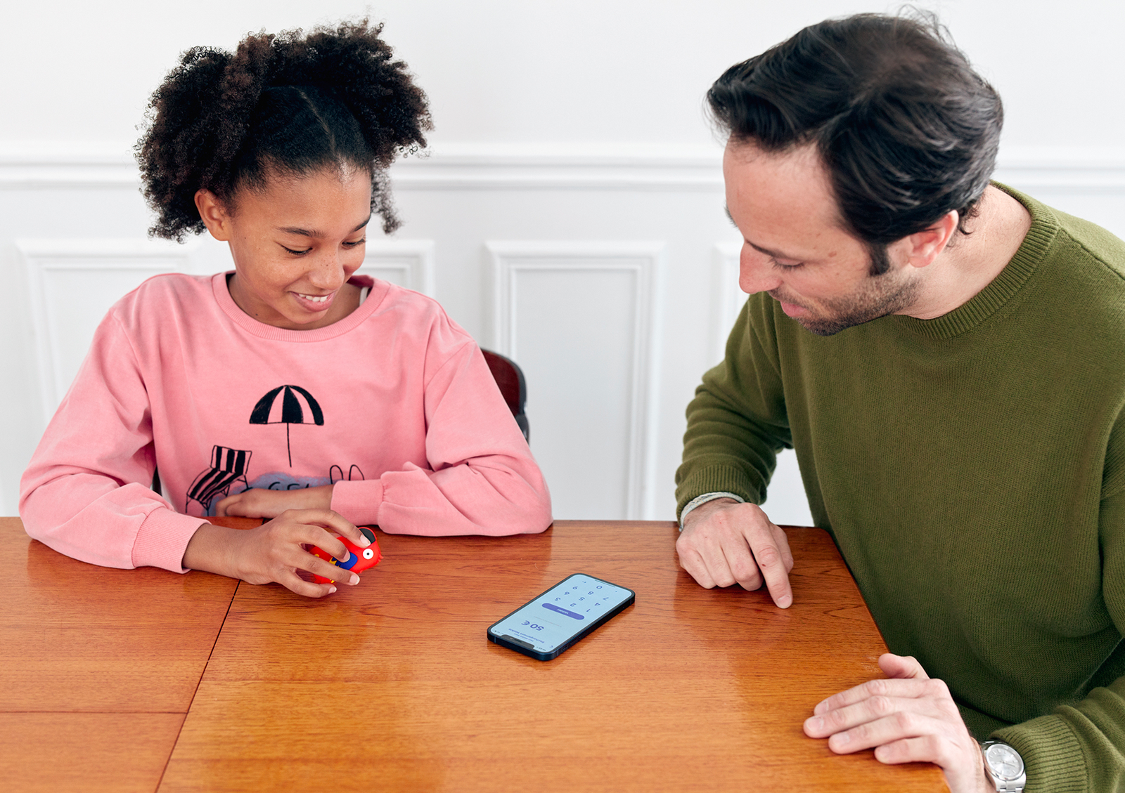 Un parent et un enfant ajoutant de l'argent sur l'objet connecté en forme de perroquet depuis l'application Money Walkie