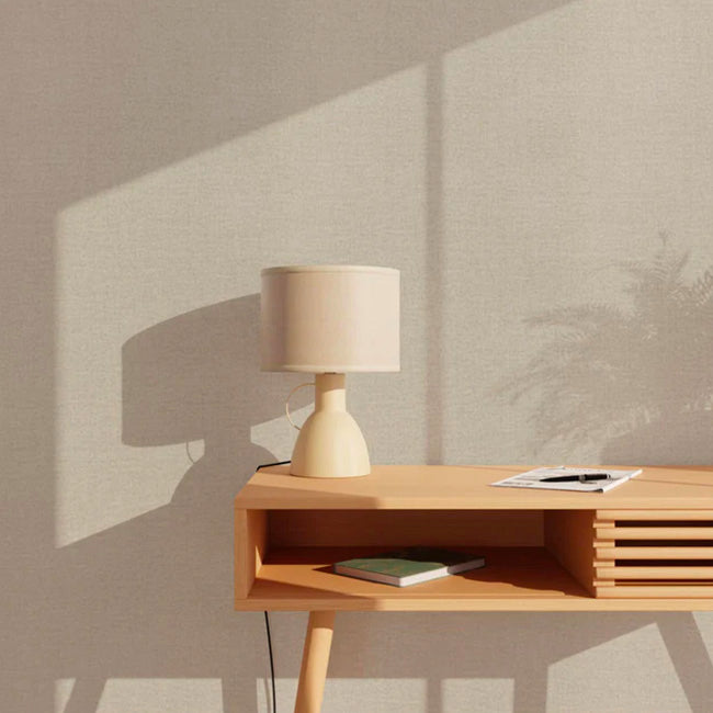Papier peint beige uni couleur lin appliqué au mur, bureau en bois et lampe à poser style amphore