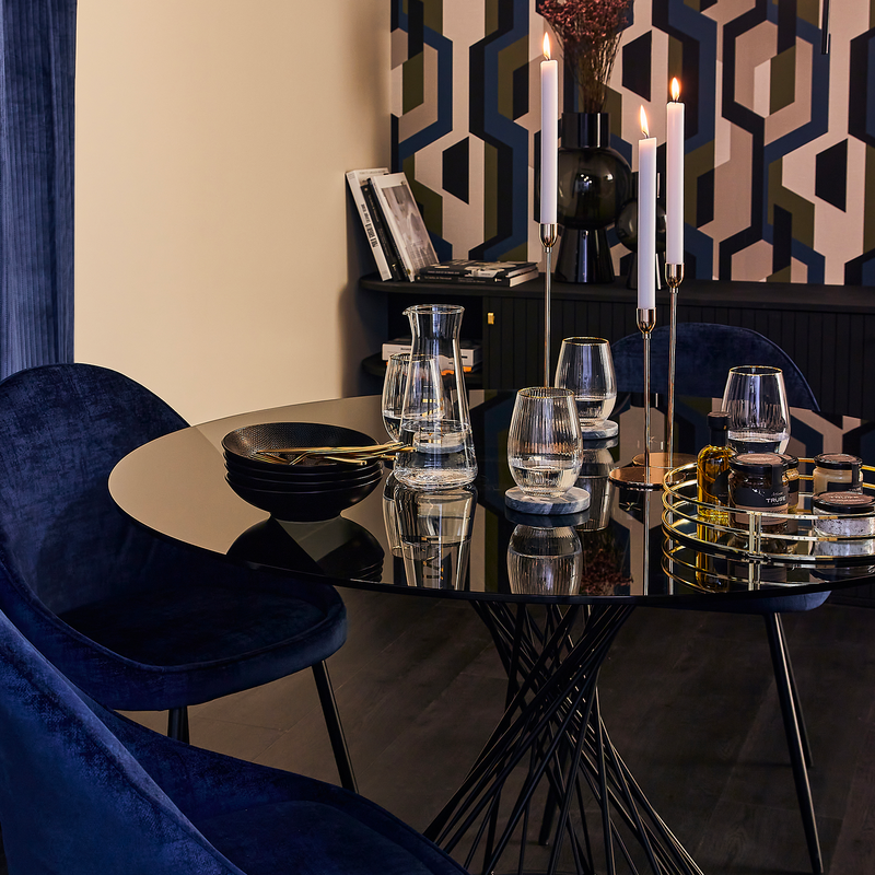 Table à manger ronde avec verres, vaisselle et déco, entourée de chaises en velours bleu