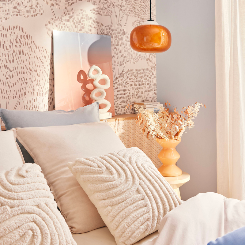 Coussins blancs posés sur le lit dans une chambre aux couleurs pastel, beige, bleu ciel et orangé