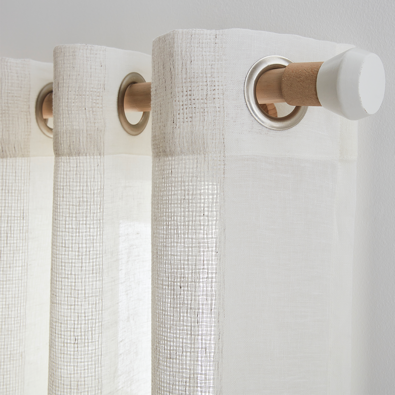 Photo cadrée sur le haut d'un voilage blanc installé sur une barre à rideau en bois clair